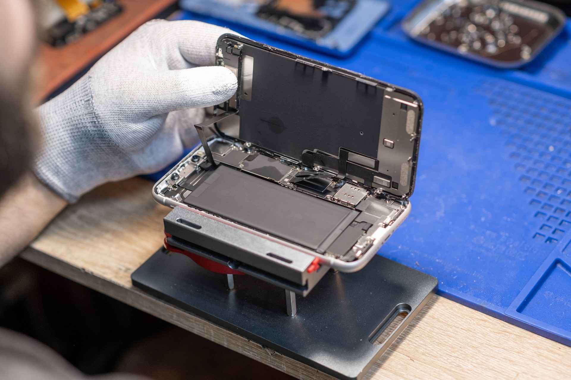 A technician carefully replaces a smartphone battery while working in a well-equipped tech repair workshop